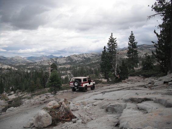 White and red SUV with spare tire on rear door, driving on a rocky, mountainous terrain