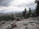 1991 Ford Bronco - A two-tone SUV navigates a challenging rocky path with a vast, forested mountain landscape under a cloudy sky.