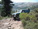 1991 Ford Bronco - A green 1991 Ford Bronco navigates a , rocky trail with a scenic lake and mountains in the distance.