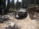 1991 Ford Bronco - An off-road vehicle carefully maneuvers through a challenging, rocky terrain with dense forest surroundings.