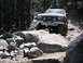 1991 Ford Bronco - A lifted Ford Bronco navigates a challenging, rocky off-road path through a forest.