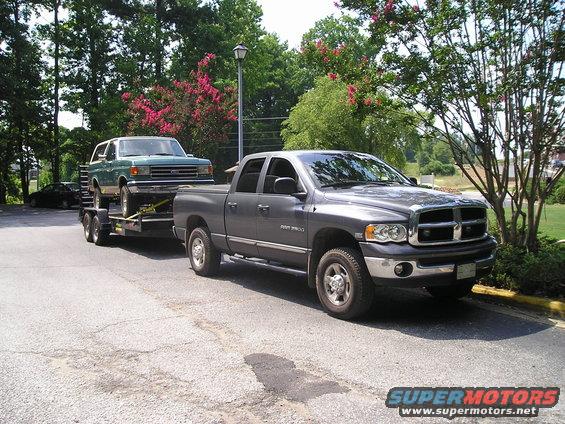 Green 1990s Ford Bronco on a trailer, towed by a gray Dodge Ram pickup truck