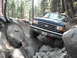 1991 Ford Bronco - A dark-colored Ford truck is shown off-roading on a steep, rocky path surrounded by trees.