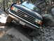 1991 Ford Bronco - A black Ford Bronco is shown off-roading on a rocky trail, with its front passenger side tire elevated.