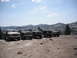 1991 Ford Bronco - Several off-road vehicles are parked in a line on a dusty mountain road under a partly cloudy sky.