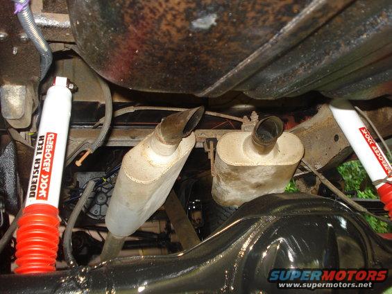 Underside of a vehicle showing dual mufflers, red and white Doetsch Tech shock absorbers, and a differential