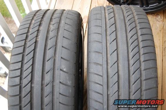 Two car tires side-by-side on a wooden surface. A black rim is visible in the upper right