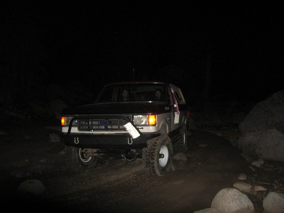 1989 Ford Bronco with a brush guard and off-road tires on a dirt path at night