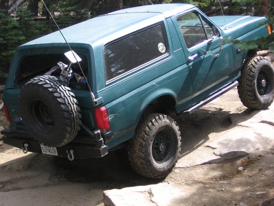 Teal 1989 Ford Bronco with spare tire on rear, off-roading on rocks
