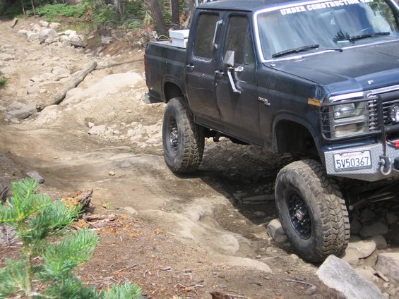 Dark blue Ford F-Series pickup truck with lifted suspension driving on a rocky trail. License plate reads 5V50367