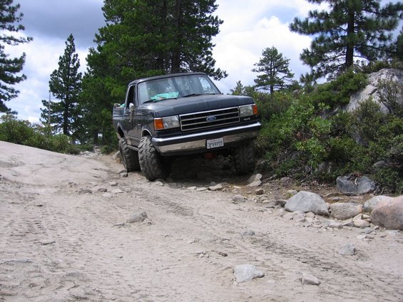 Dark blue 1987 Ford F-150 pickup truck with lifted suspension on a rocky, dirt road