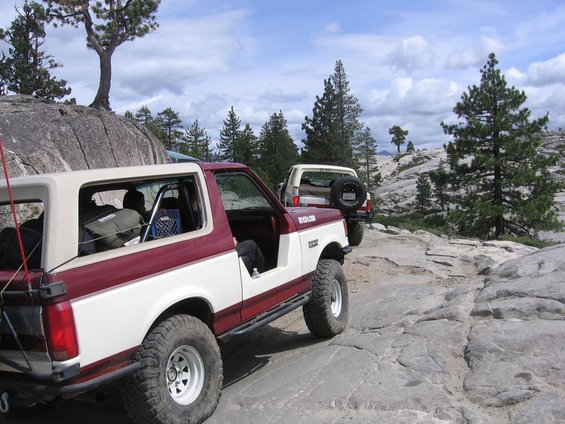 Two-tone maroon and white 1989 Ford Bronco with off-road tires parked on a rocky surface