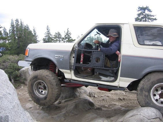 1989 Ford Bronco with aftermarket doors and roll cage navigating rocky terrain
