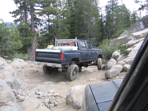 Dark blue Ford F-Series pickup truck with a rack on top, driving off-road on a rocky trail