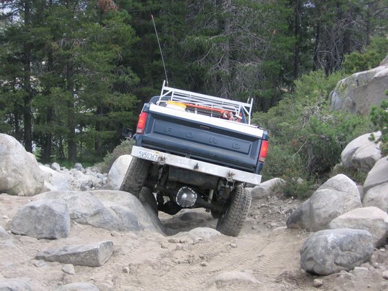 Dark blue Ford pickup truck navigating a rocky trail, rear view