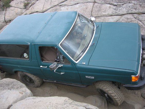 Green SUV with a removable hardtop, off-roading over rocks and sand. Visible badge reads 'BRONCO'