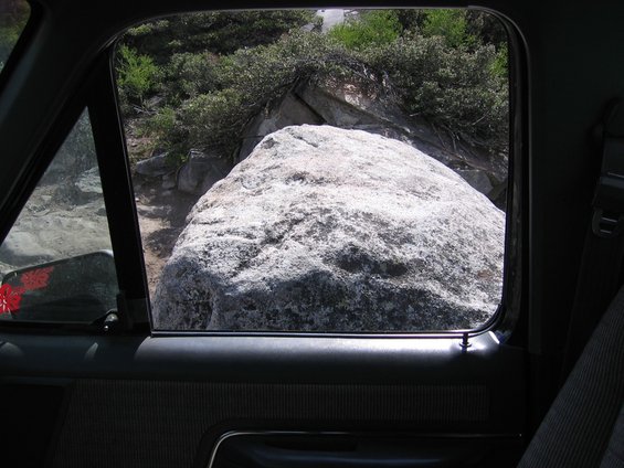 view from inside vehicle looking out window at large rock on a dirt path with bushes