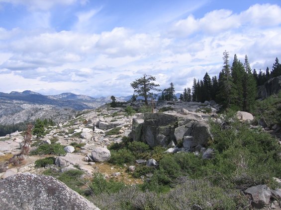 Rocky mountain landscape with scattered trees under a cloudy blue sky