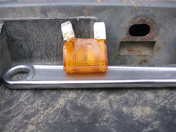 Orange automotive fuse on a metal wrench, resting on a textured surface