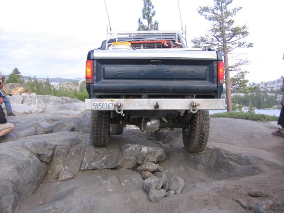 Dark blue Ford truck with a silver bumper and a ladder rack, driving over rocks
