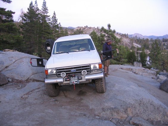 White Ford truck with winch on rocky terrain, driver's door open
