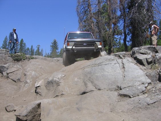 Ford Bronco climbing over rocks on a trail. Two people watch from the side