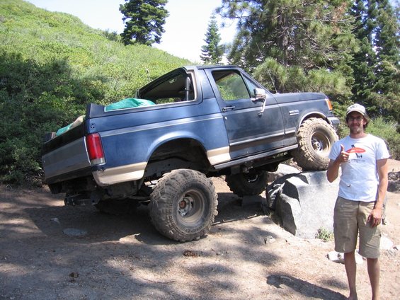 Blue Ford Bronco with tan trim, lifted, on rocks, with a man giving a thumbs up