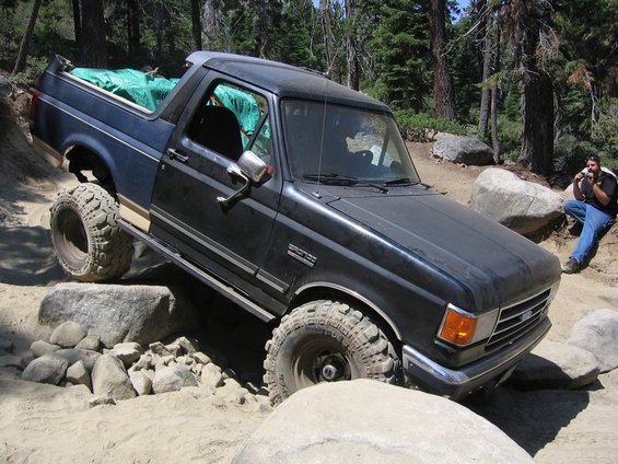 Black Ford Bronco with lifted suspension navigating rocks on a trail. Bronco badge visible on the fender