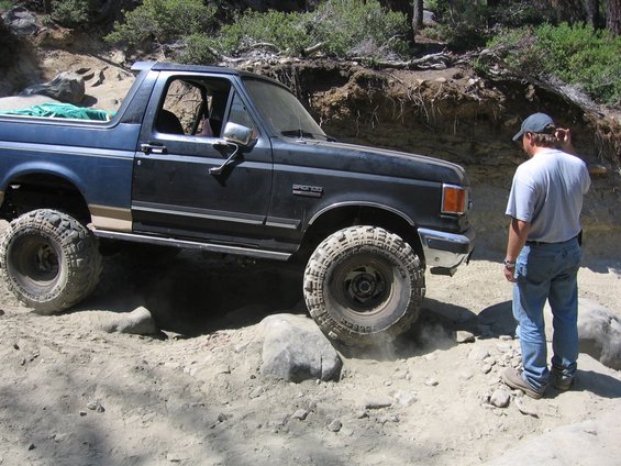 1989 Ford Bronco navigating a rocky off-road path with a person watching