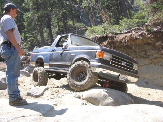 Guy watches a 1989 Ford Bronco crawl over rocks on a trail