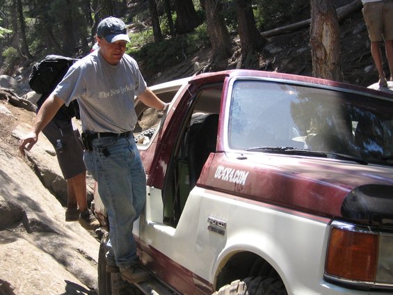Red and white 1989 Ford Bronco off-roading with a man stepping out
