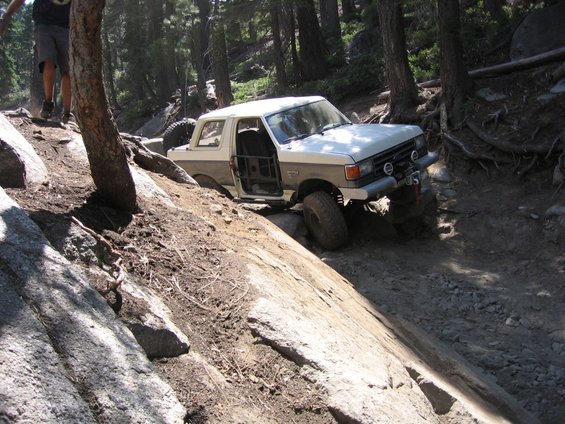 1989 Ford Bronco navigating a steep, rocky off-road trail with the driver's door open