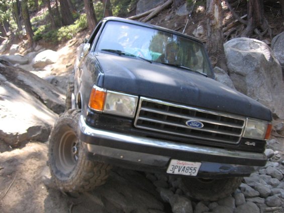 Black Ford truck with a lifted suspension driving over rocks
