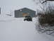 1990 Ford Bronco - A white and black Ford F-Series truck is partially buried in snow in front of a large metal building.