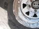 1991 Ford Bronco - Close-up of a damaged white steel wheel and tire, with visible chipping and a dent in the rim.