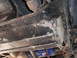 1991 Ford Bronco - The undercarriage of a vehicle is visible, a blue oil filter and heavily weathered frame components.