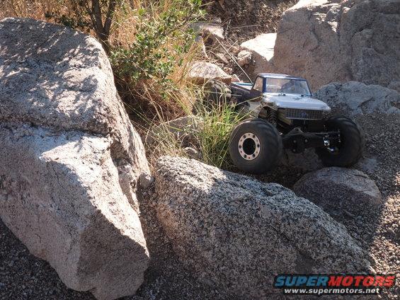 RC truck with big tires crawling over rocks and dry grass
