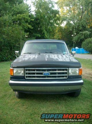 1987 Ford Bronco front view, dark blue, faded paint on hood, chrome bumper, parked on grass