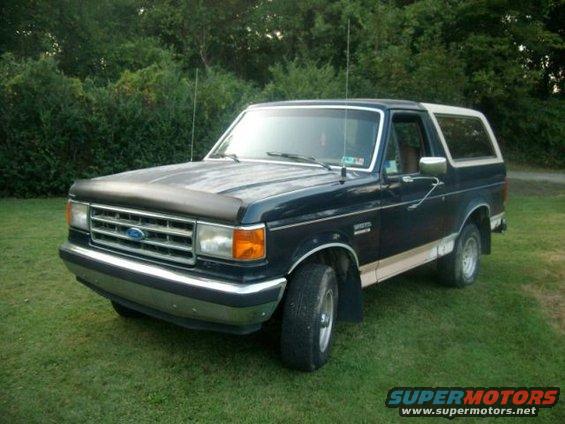 Dark blue 1987 Ford Bronco with white top, parked on grass