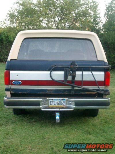 1987 Ford Bronco rear view, blue and red stripe tailgate, tan roof, spare tire carrier, license plate EYL-6069
