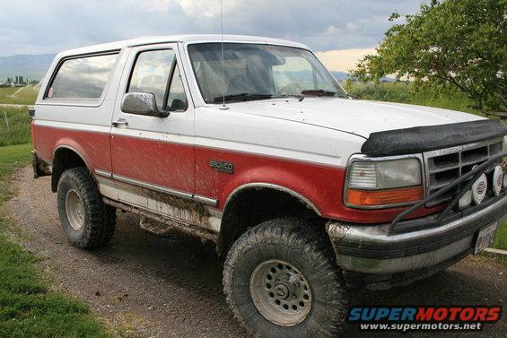 White and red Ford Bronco with off-road tires, mud-splattered, parked on a dirt road
