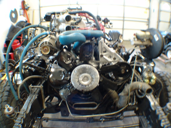 Engine assembly with blue hoses and silver fan. Some vehicle frame visible