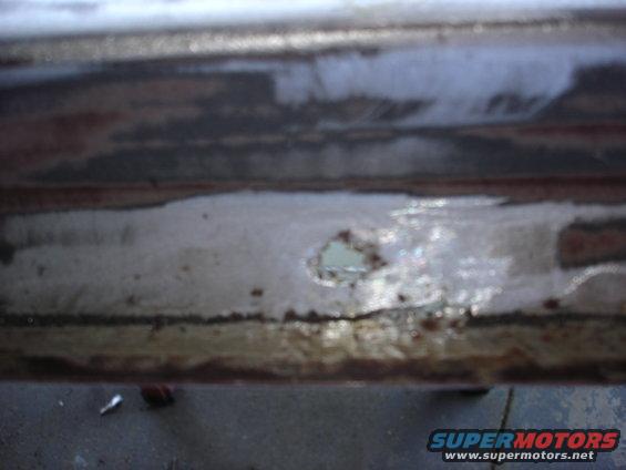 rusted metal panel with a hole showing light blue underneath, Supermotors.net logo visible