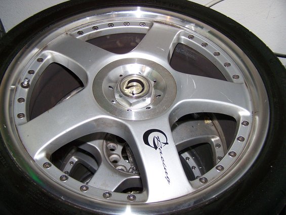 Close-up of a silver five-spoke alloy wheel with a black tire. Text on the wheel reads 'Racing'