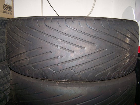 Tire with directional tread pattern, stacked on another tire. Box with 'ENKEI' visible