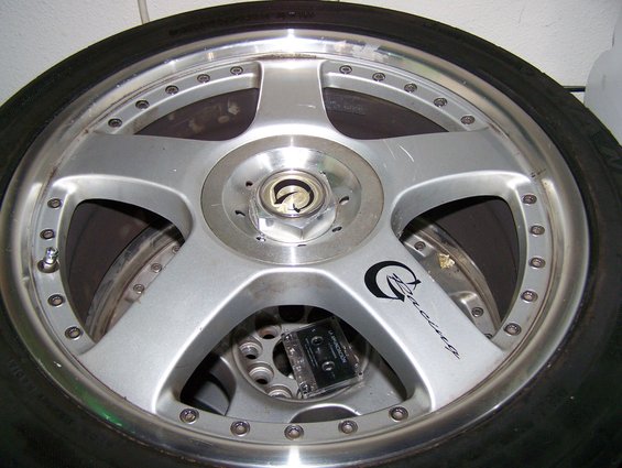 Silver five-spoke aftermarket wheel with black racing logo and cassette tape inside