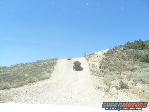 Off-road vehicle driving up a steep dirt hill under a clear blue sky