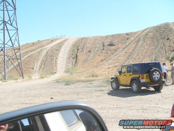 Yellow Jeep Wrangler parked on dirt road with a hill in background