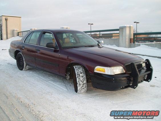 Maroon Ford Crown Victoria with a black push bar parked in snow. Front passenger tire is covered in snow