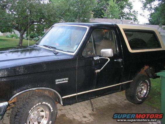 Black Ford Bronco with a tan top, seen from the side at a 3q-front angle. The vehicle has a chrome trim line and appears to be in fair condition